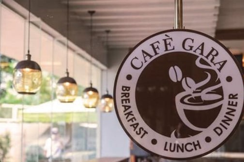 The Café Gara seal hanging in the café, with globe lights and a window beyond.